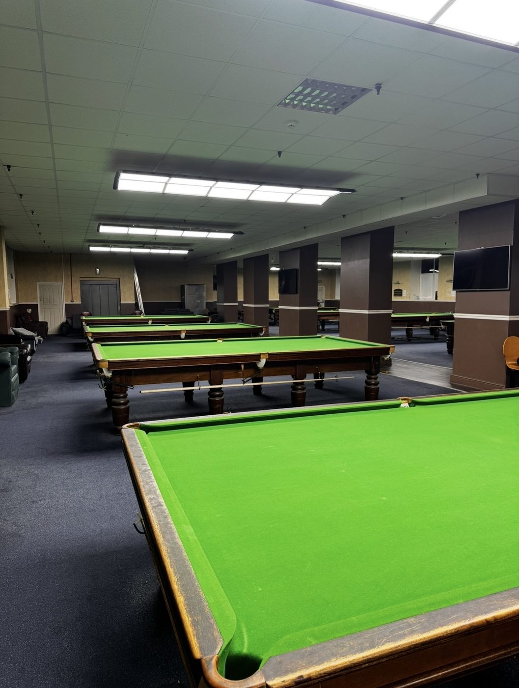 A diagonal row of full-size snooker tables under strip lighting in the main hall at Dewsbury Snooker Centre.