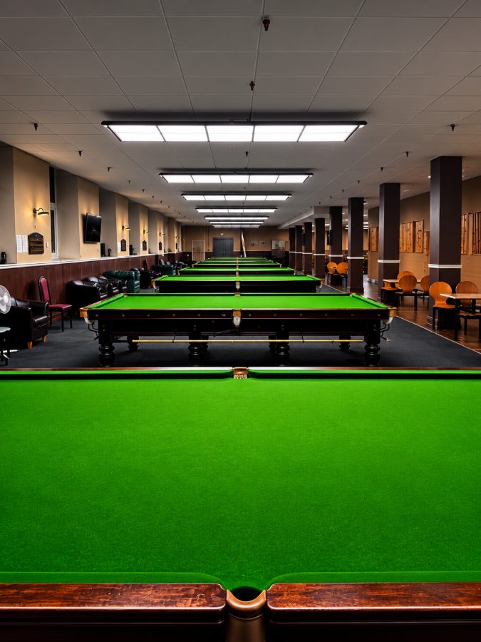 The length of the club from behind a table pocket, tables in a line with leather armchairs down one side.