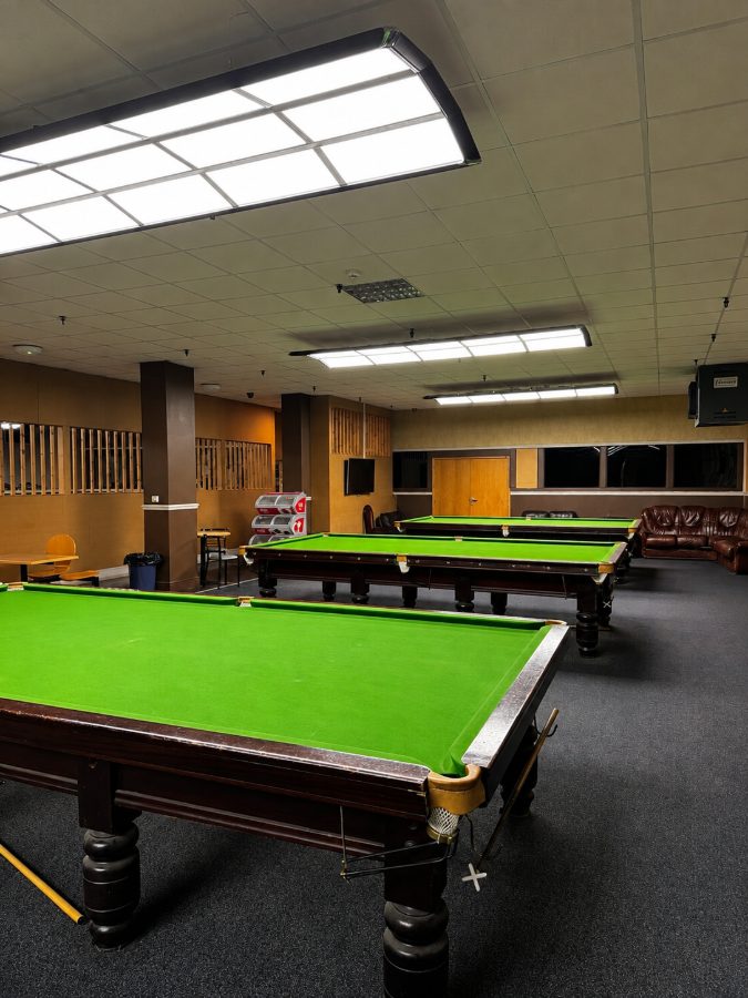 Snooker tables at the far end of the club, with leather seating and a drinks machine against the back wall.